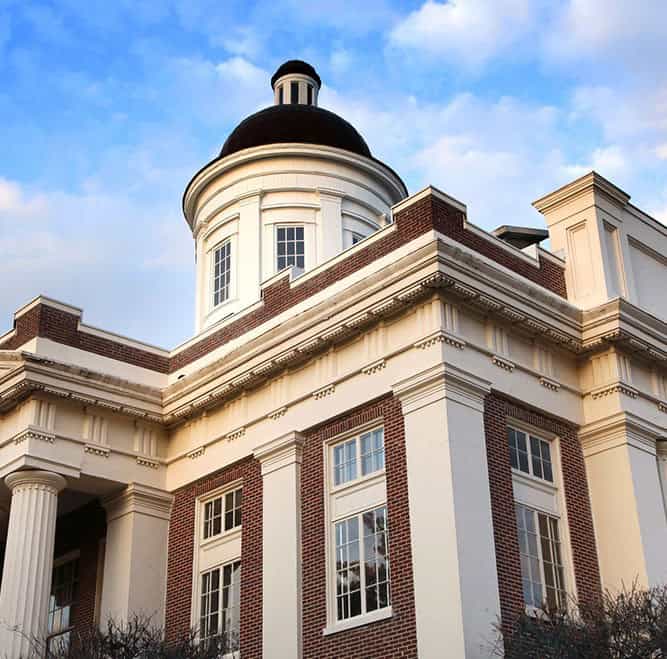 A building with a dome and columns, featuring red brick and white accents, against a partly cloudy sky.
