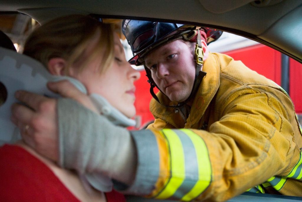 A firefighter assists a woman by applying a neck brace while she sits in a car.